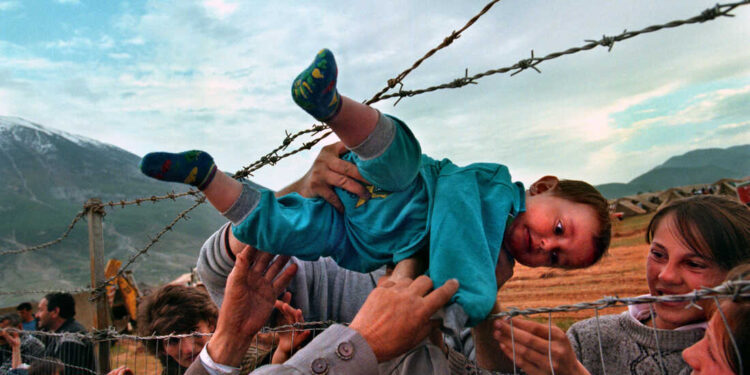 Family members, reunited after fleeing Kosovo, pass 2-year-old Agim Shala through the barbed wire fence into the hands of his grandparents at a camp in Albania. The photo was taken on March 3, 1999.